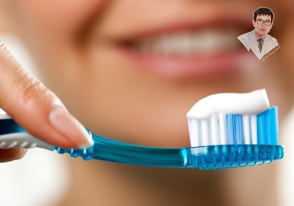 "Chăm sóc răng miệng đúng cách, ngăn ngừa tụt nướu hiệu quả!" Hình ảnh bàn chải đánh răng với kem đánh răng được giữ trên tay một người phụ nữ đang mỉm cười, thể hiện việc chăm sóc răng miệng thường xuyên giúp phòng ngừa tụt nướu răng cửa.